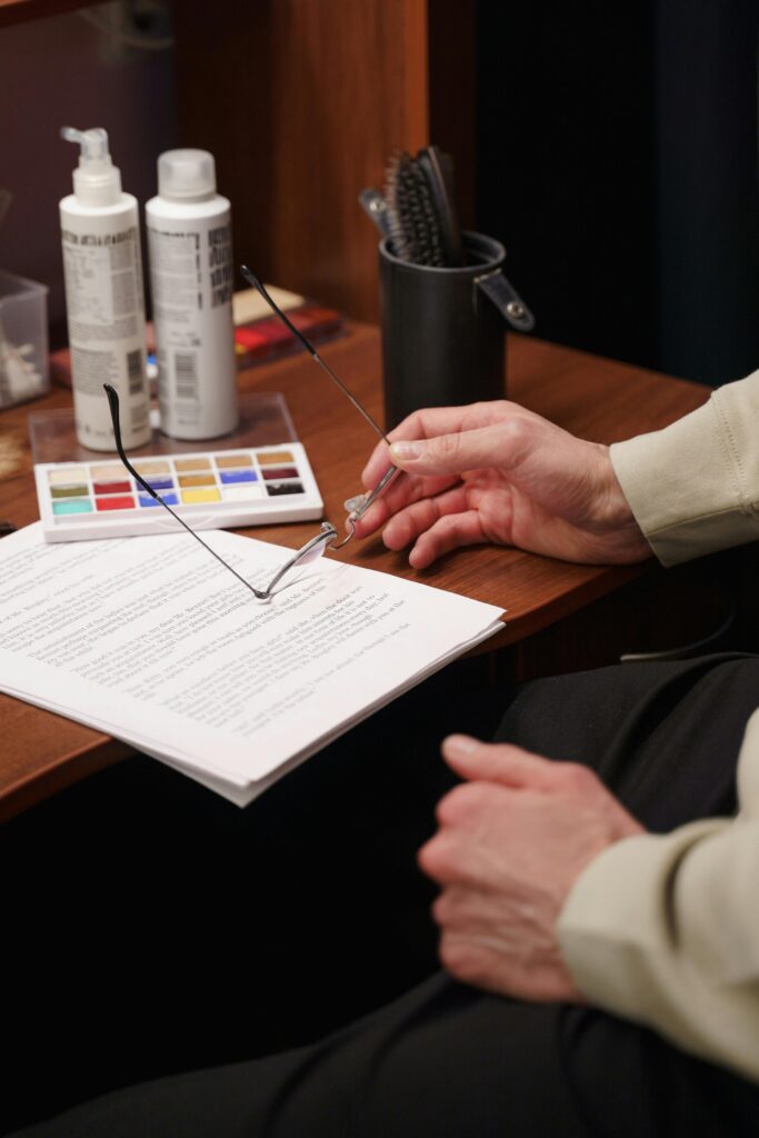 Close-up of a male actor reviewing a script with glasses, backstage at a theater dressing room.